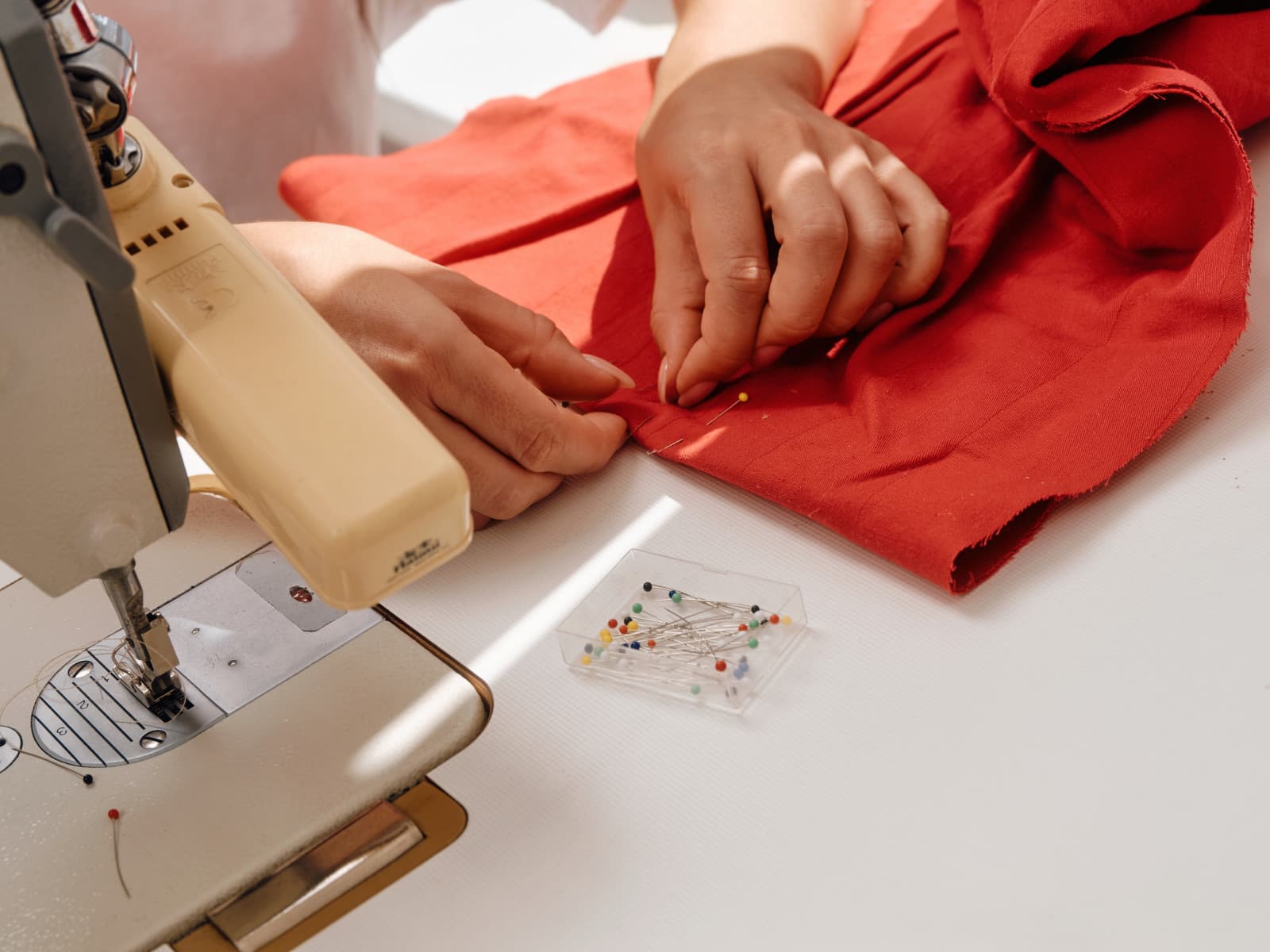 Hands pinning red fabric at a sewing machine