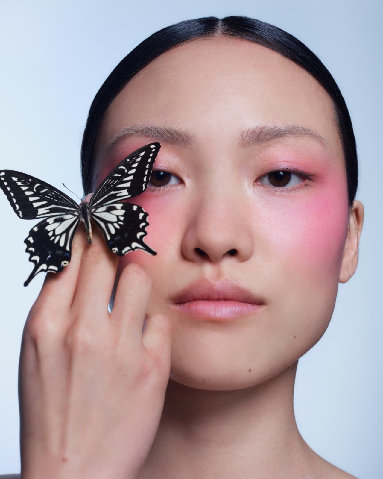 A model with pink blush holding a swallowtail butterfly