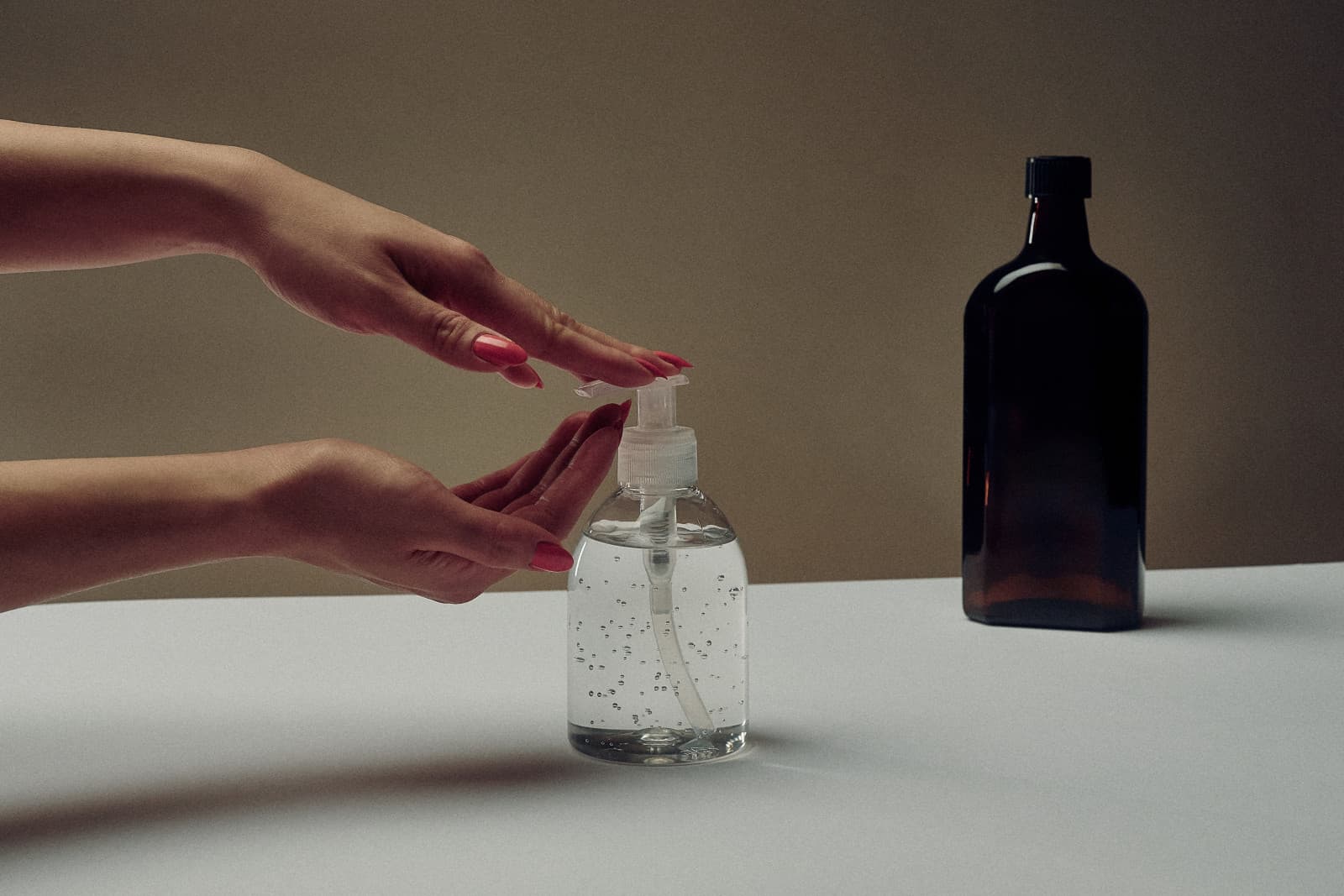 A hand reaching for a clear pump bottle beside a dark glass bottle