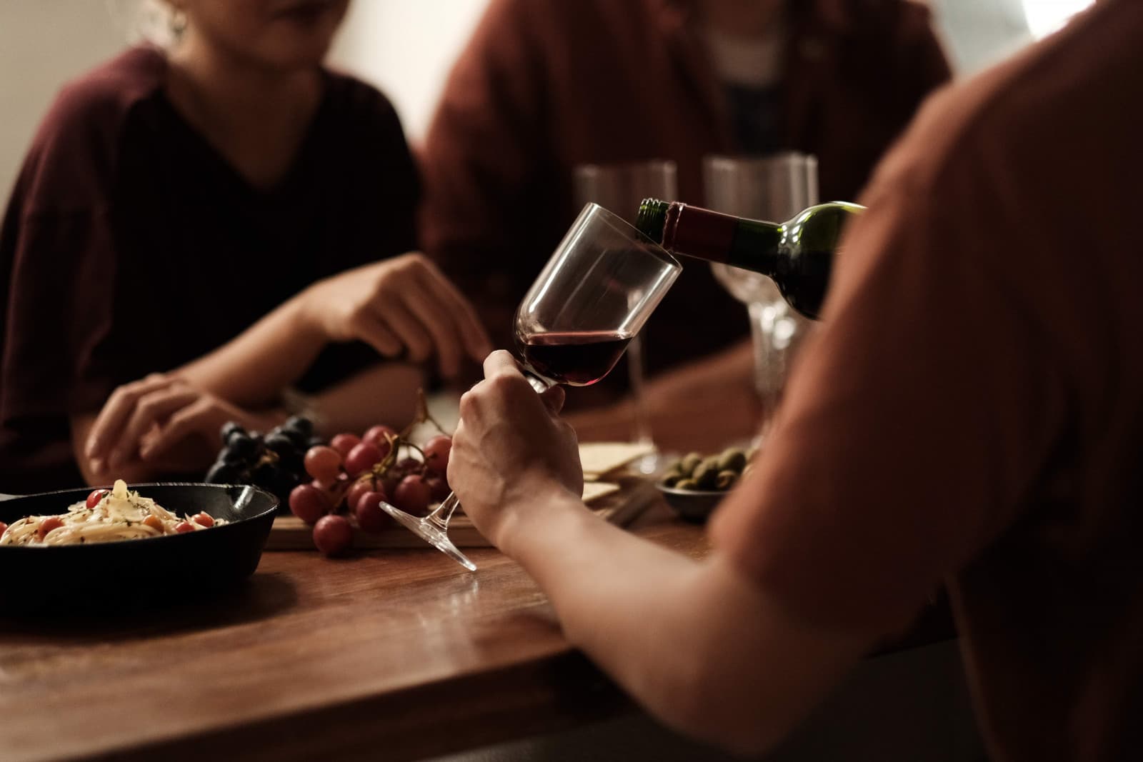 A dinner table with pasta, grapes, and a glass of red wine